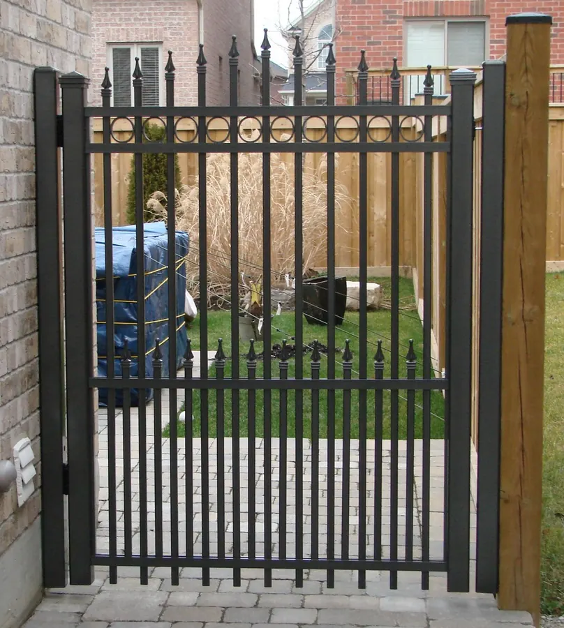Tall black aluminum pedestrian spear-top gate between brick row houses