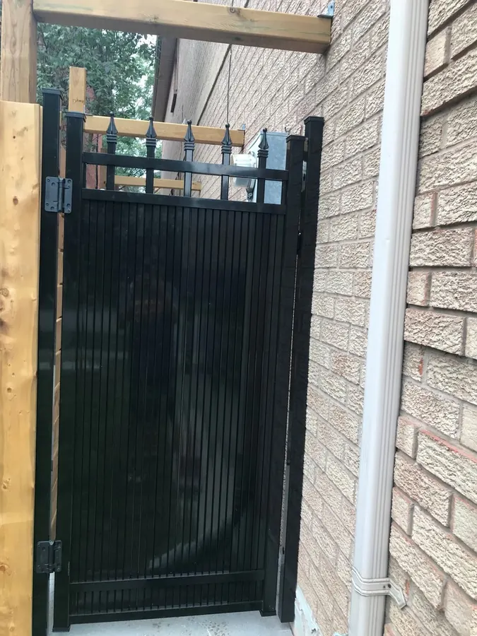 Tall solid black aluminum gate against stone-veneer wall (privacy install)